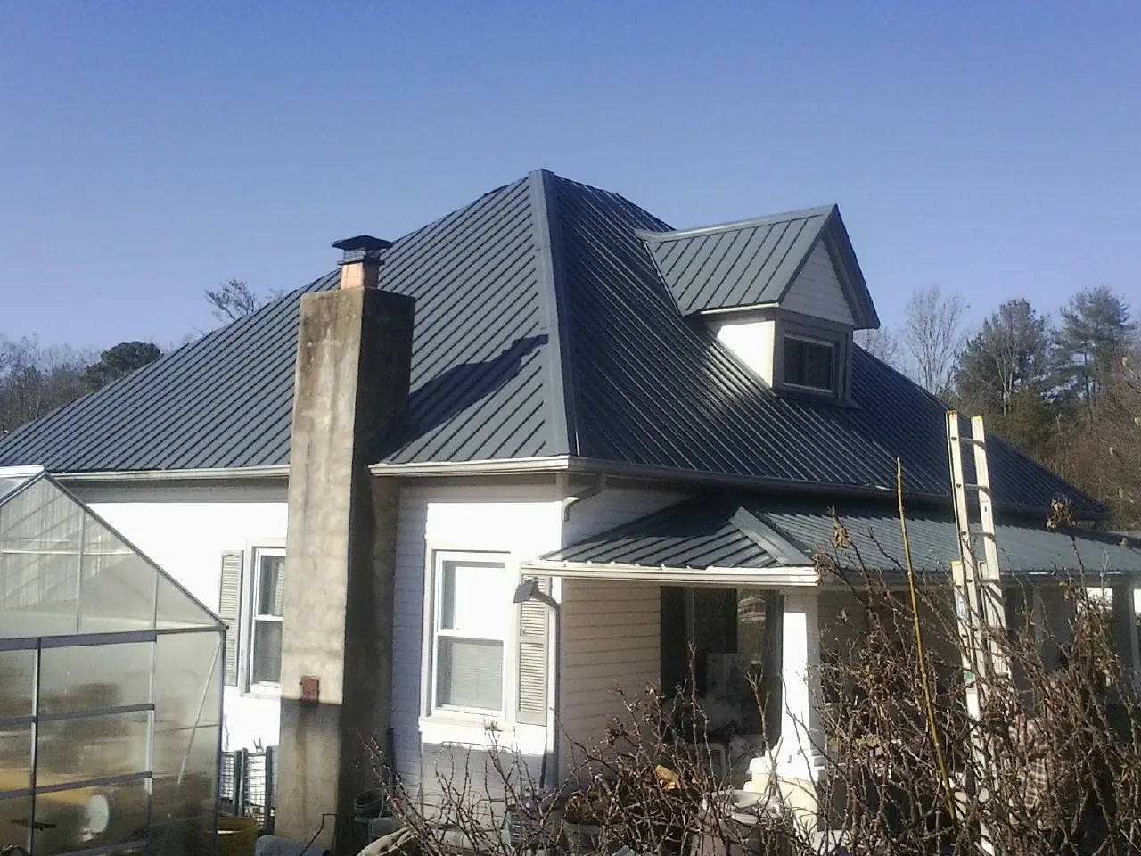 Dark blue standing seam metal roof on a white farmhouse with dormer — Slate & Tile Roof Repair by Roofing Brothers in Canova