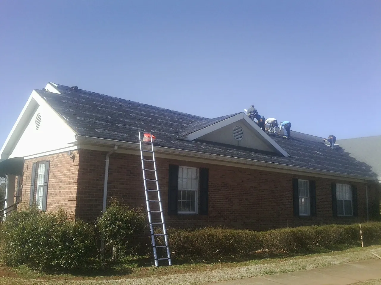 Crew tearing shingles off a brick ranch roof with a ladder set — Emergency Roof Repair work by our crew in Canova
