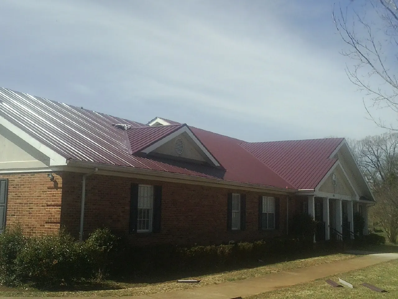 Red metal roof with gabled entries on a long brick building, from a Hail Damage Roof Repair job in Canova