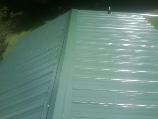 New green metal panels meeting at the ridge of a roof — Flat Roof Repair work by our crew in Canova
