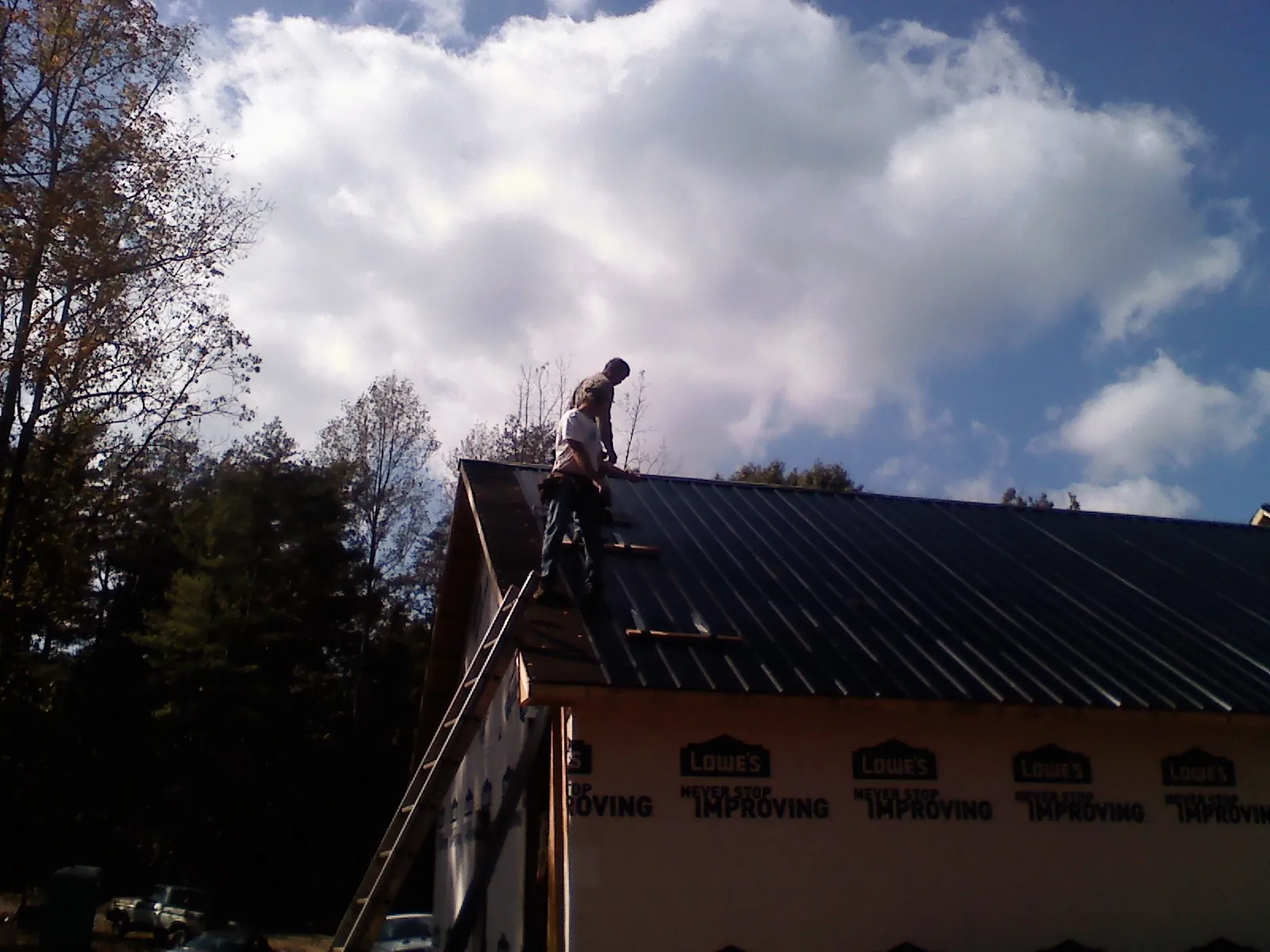 Roofer fastening dark metal panels high against a cloudy sky, from a Roof Inspection job in Canova