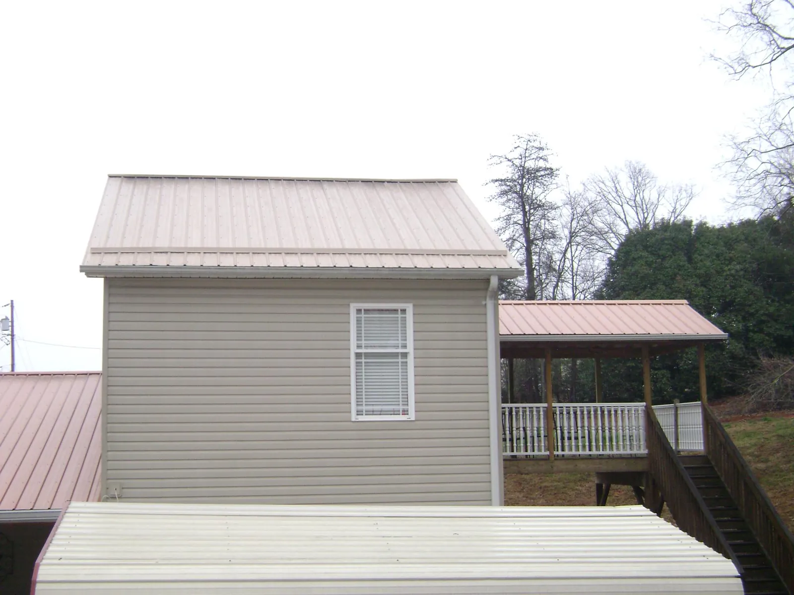 Tan metal roofs on a two story addition and attached porch, from a Roof Replacement job in Canova